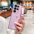 Purple smartphone with a gold-trimmed case and a heart-shaped wrist strap.