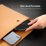 Slim wireless charging pad being inserted into a tan leather sleeve alongside a smartphone.