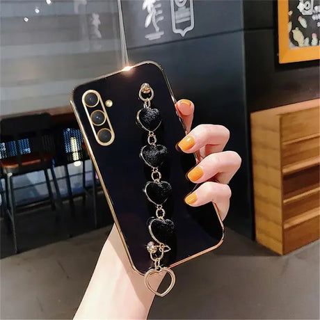 Smartphone with a black case featuring a dangling heart-shaped charm accessory.