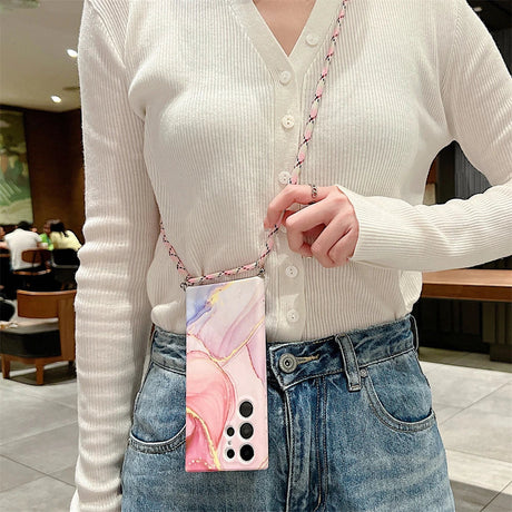 Smartphone case with a pink marble design and a chain strap worn as a crossbody accessory.