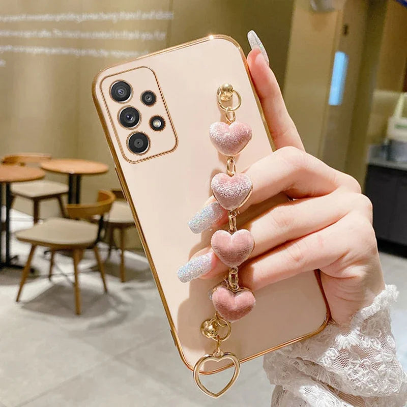 Smartphone with a pink case and heart-shaped charm accessory held by a hand.