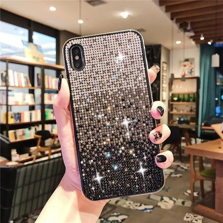 Sparkly, rhinestone-encrusted phone case held by a hand with dark nail polish.