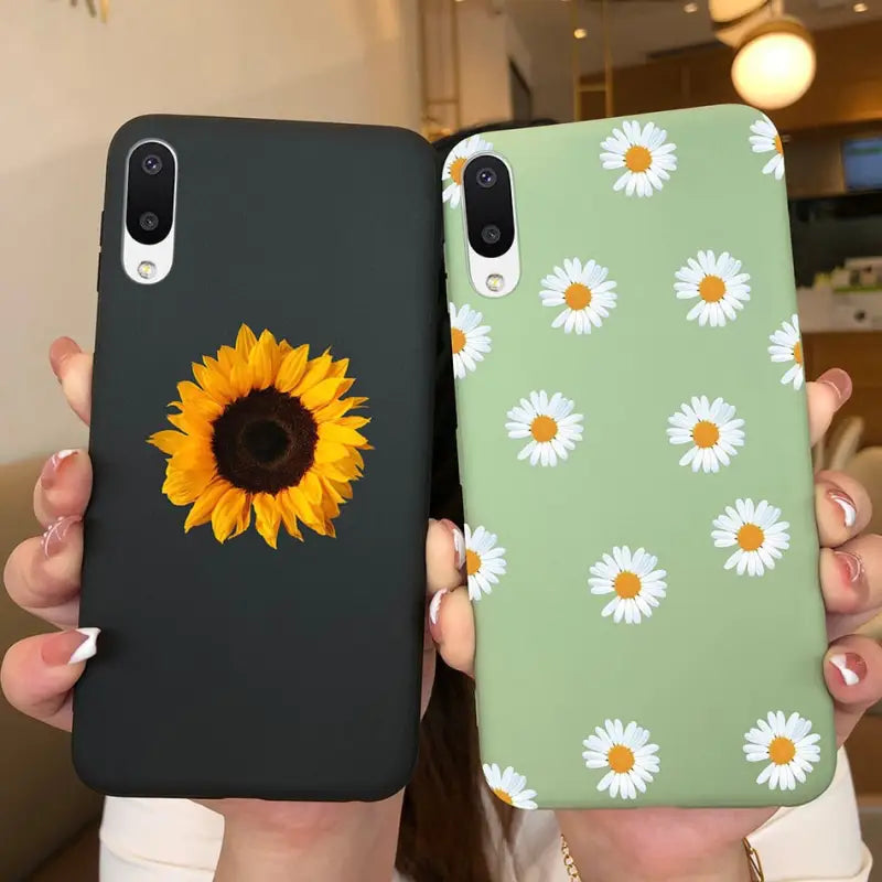a woman holding up two iphone cases with sunflowers on them