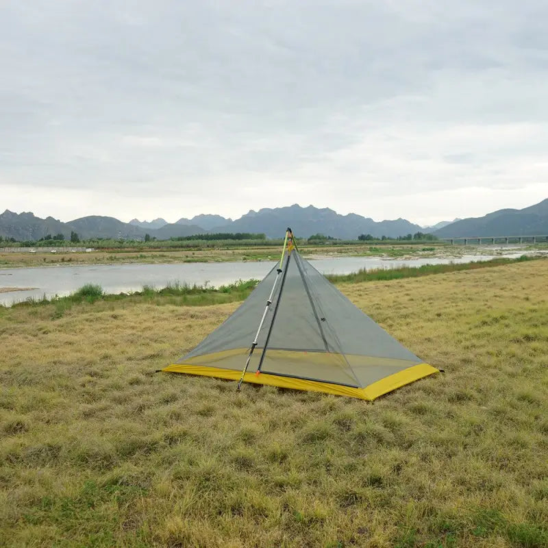 a tent pitched up on the grass by a river