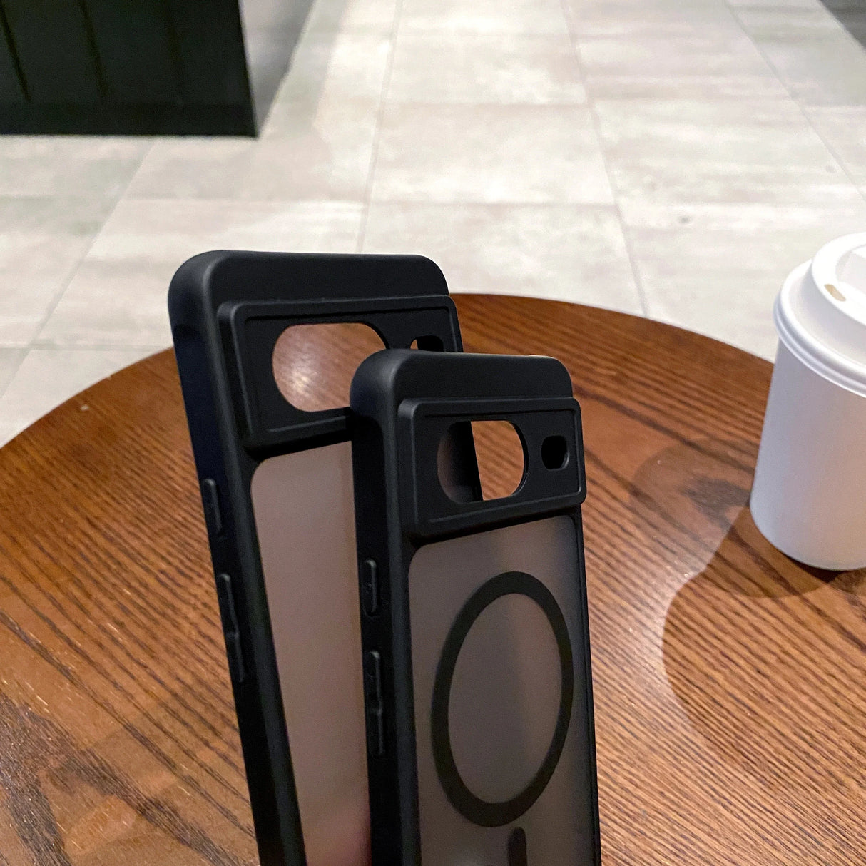 Two black smartphone cases with circular cutouts on a wooden surface.