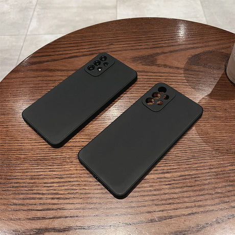 Two black smartphone cases with camera cutouts on a wooden surface.