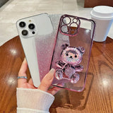 Two iPhone cases, one white with glitter and one purple with a cute bear decoration.