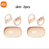 Two pairs of beige wireless earbuds with ear hooks and their matching charging cases.
