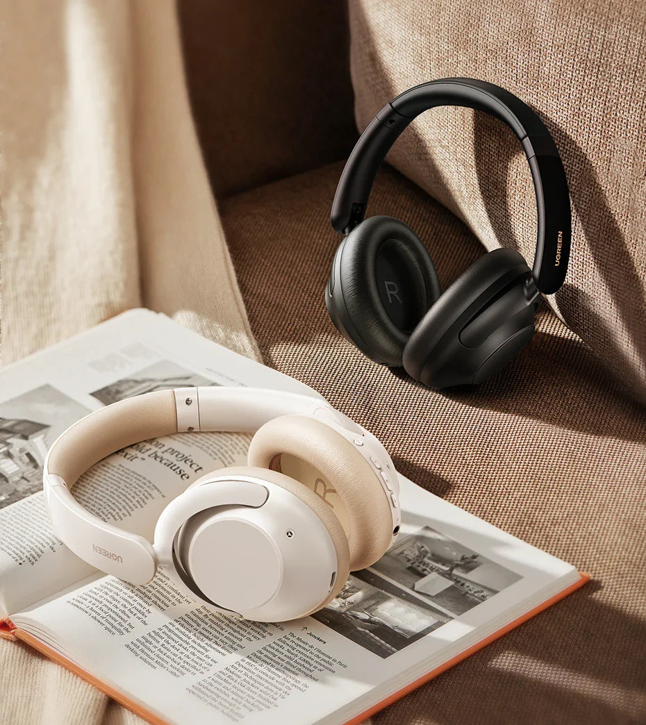 Two pairs of over-ear headphones, one white and one black, resting on an open book.