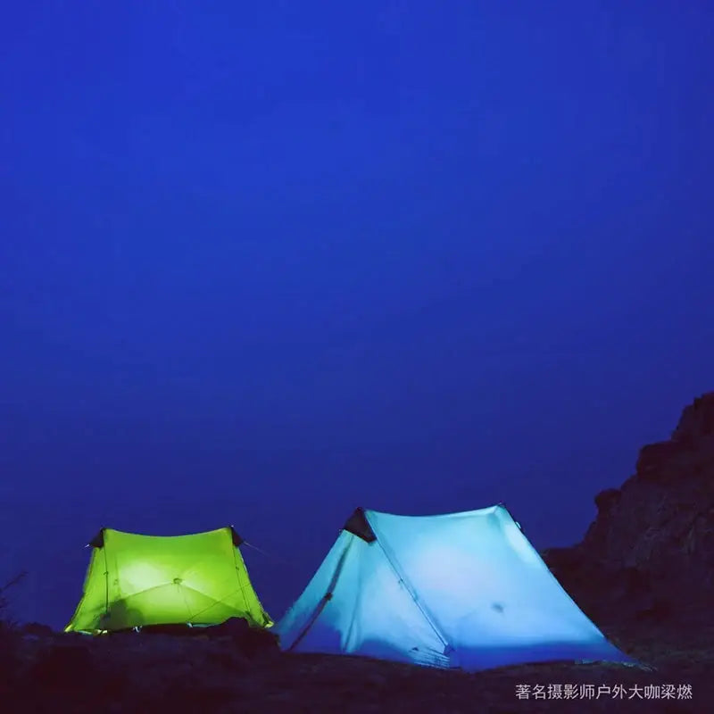 Two tents lit up at night on a rocky mountain