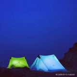 two tents lit up at night on a rocky mountain