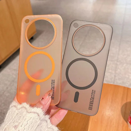Two transparent phone cases, one orange-tinted and one gray-tinted, featuring circular cutouts and magnetic rings for wireless charging.