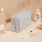 a white bag with a gold zipper and a white makeup brush