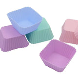 four different colored cupcake cases are lined up on a white surface