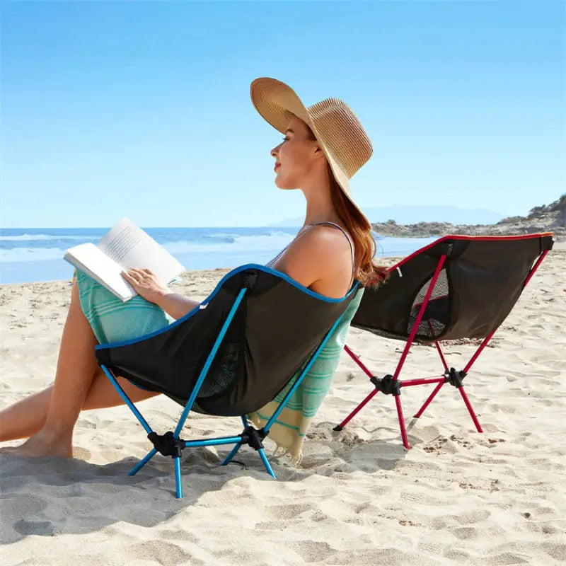 a woman sitting in a chair on the beach reading a book