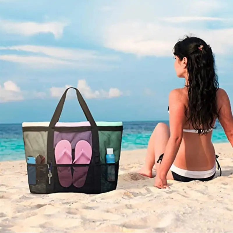 a woman sitting on the beach with a large bag