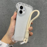 A white glitter phone case with a rhinestone camera bezel and an attached cream-colored wrist lanyard.