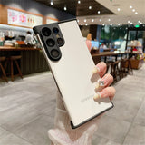 White Samsung smartphone with a black camera module and a black protective case, held by a hand with jeweled nails.