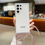 A white Samsung smartphone in a clear case with a pink lanyard.