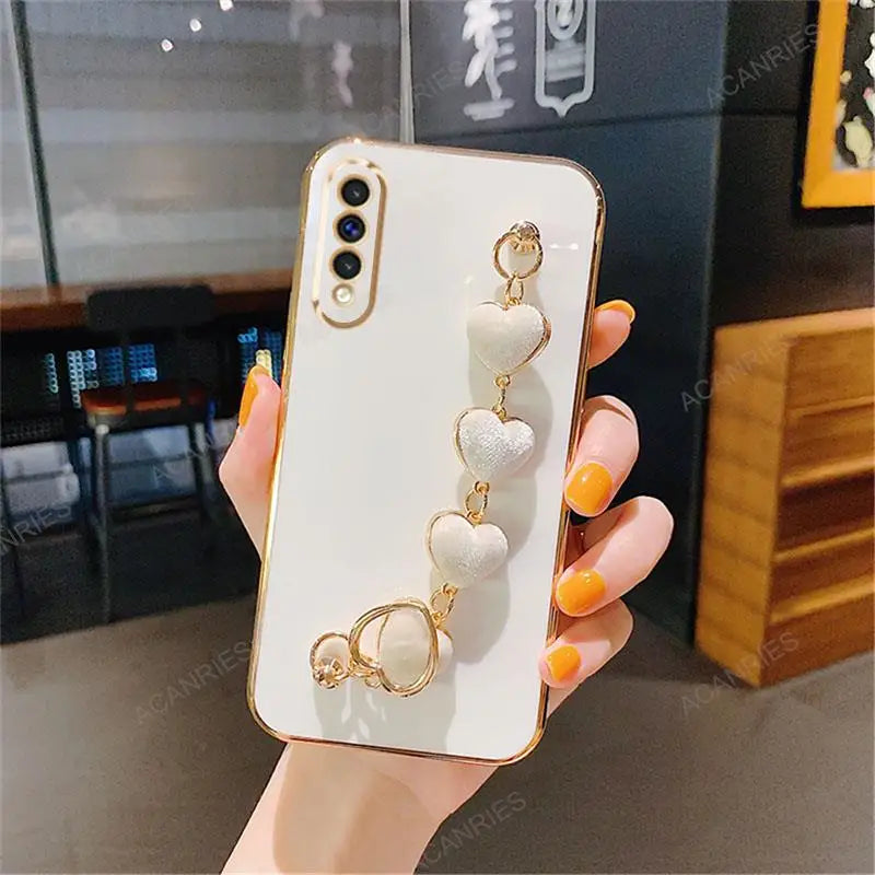 White smartphone case with decorative gold heart charms attached.