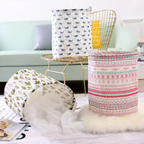 a white table topped with a white and pink patterned paper, a gold wire basket, and a white feather