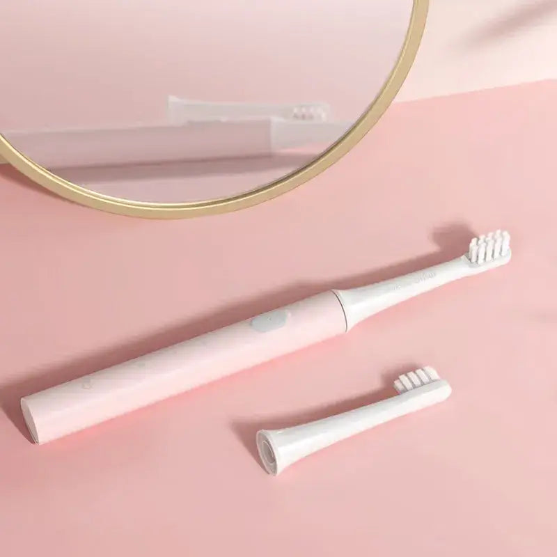 A white toothbrush and a mirror on a pink surface