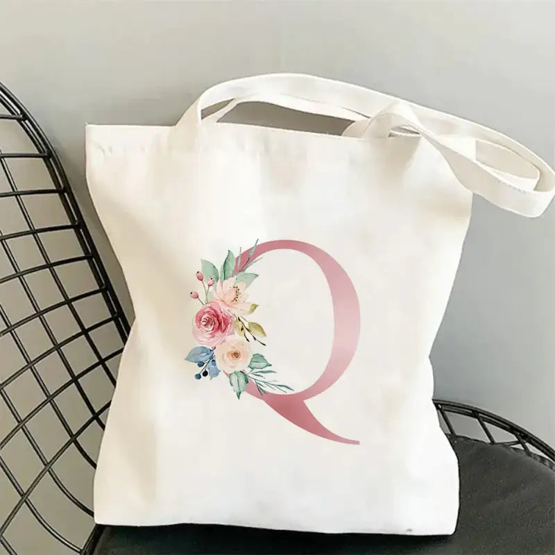 a white tote bag with a pink initial and flowers