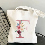 a white tote bag with a pink initial and flowers