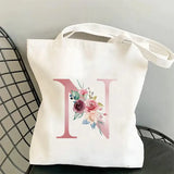 a white tote bag with a pink initial and flowers