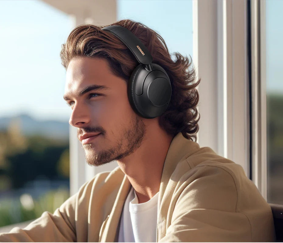 Wireless over-ear headphones worn by a person with wavy hair and facial hair.