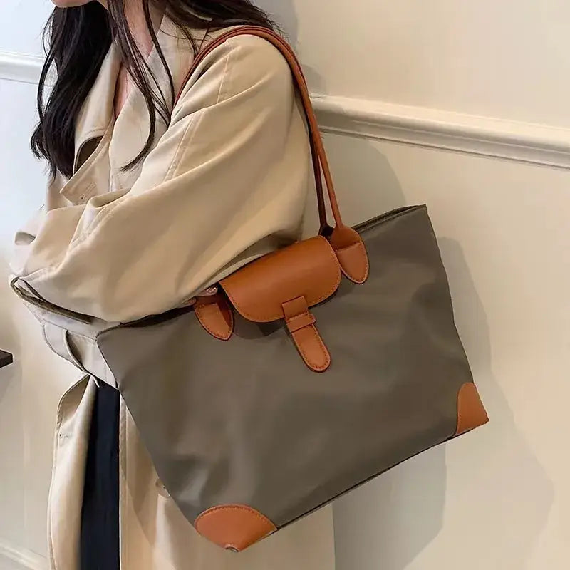 a woman wearing a beige coat and black pants holding a gray bag