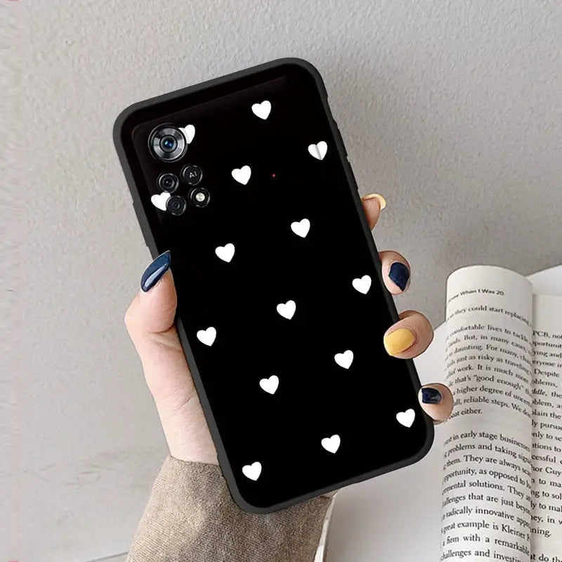 a woman holding a black phone case with white hearts on it