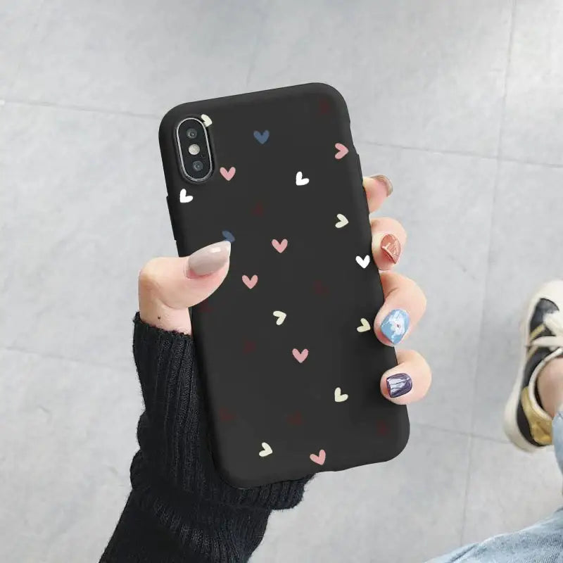 A woman holding up a black phone case with hearts on it