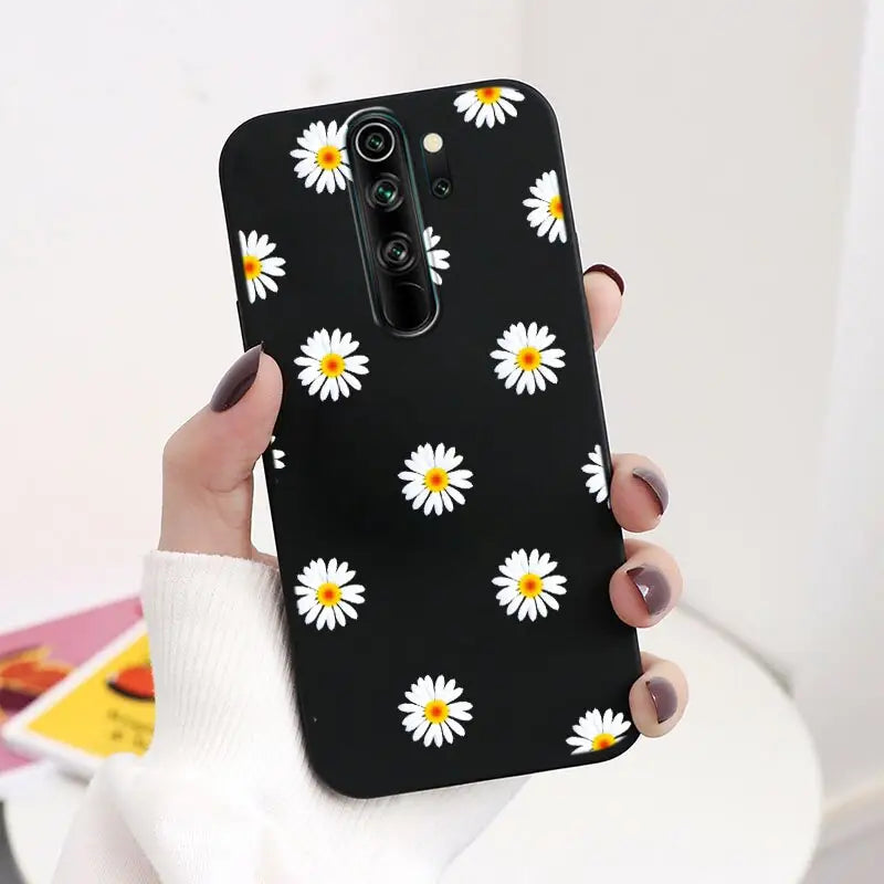 a woman holding a black phone case with white daisies on it