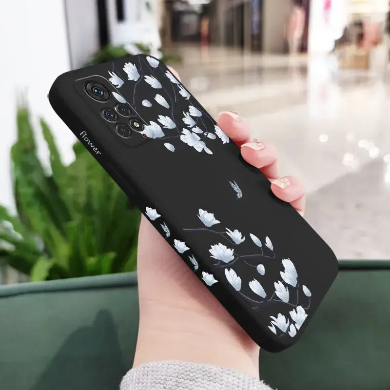 a woman holding a black phone case with white flowers on it