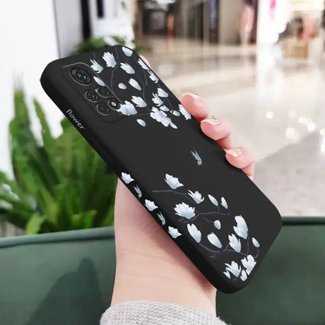 A woman holding a black phone case with white flowers on it