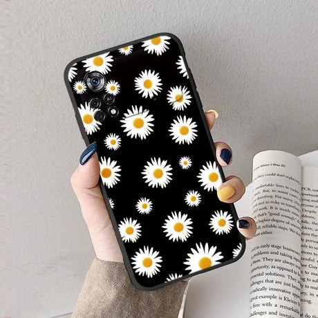 A woman holding a book and a phone case with daisies on it