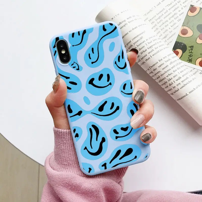 a woman holding a blue phone case with a smiley face on it