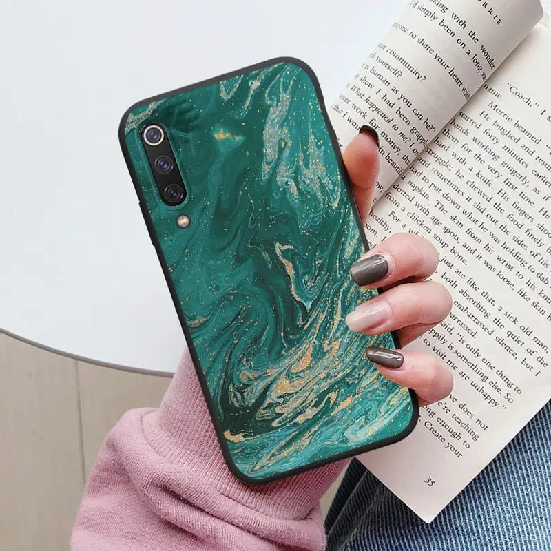 someone holding a book and a phone case with a green marbled design