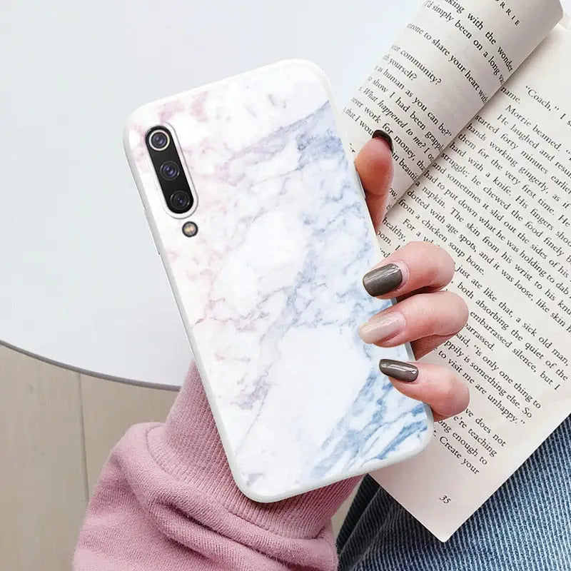 a woman holding a book and a white marble phone case
