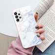 a woman holding a book and a white marble phone case