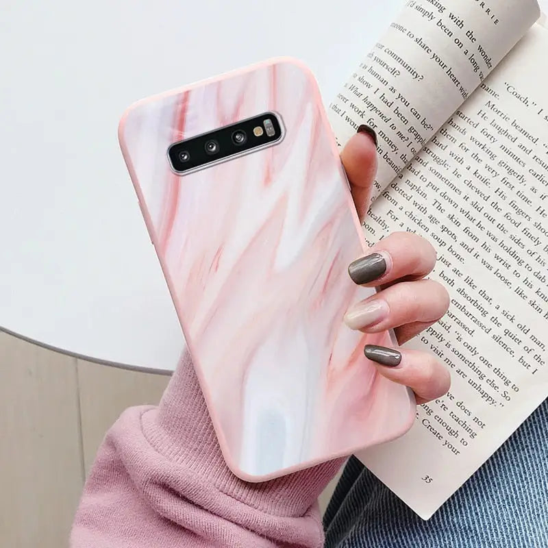 a woman holding a book and a pink marble phone case