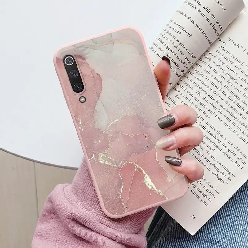 a woman holding a book and a pink marble phone case