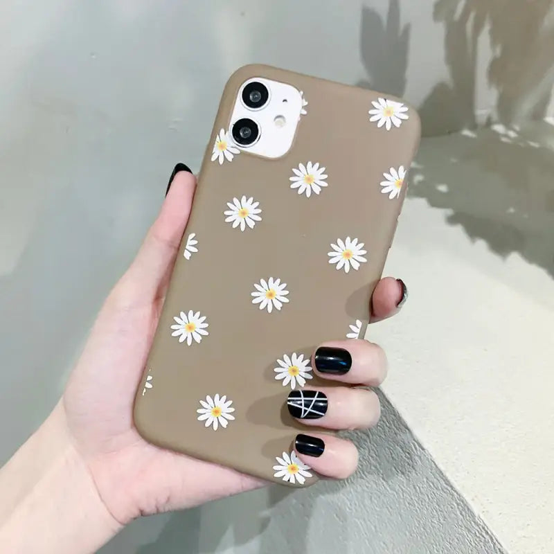 a woman holding a brown phone case with white daisies on it