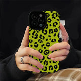 a woman holding a phone case with a green leopard print