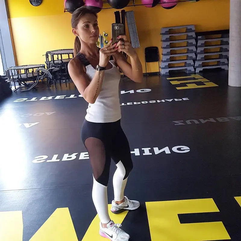 woman in a gym holding a cell phone and standing on a mat