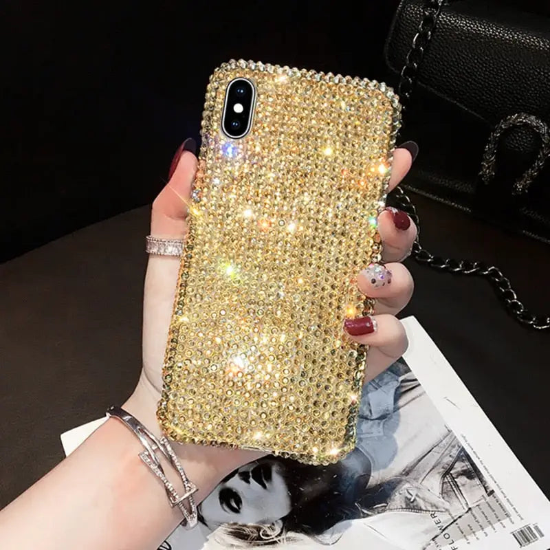a woman holding a phone case with gold crystals
