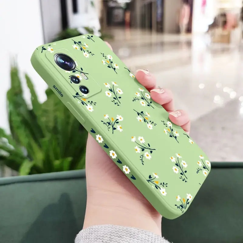 a woman holding a green phone case with white flowers on it