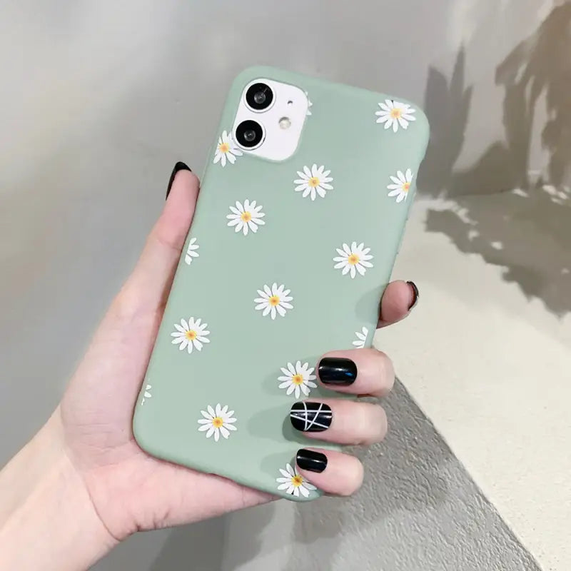 a woman holding a green phone case with daisies on it