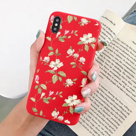 a woman holding a red phone case with white flowers on it